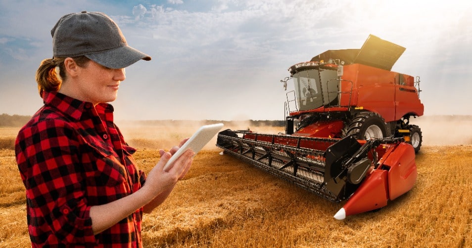 una mujer que está en un campo al lado de una máquina cosechadora, sostiene una tablet con un software gestión agrícola