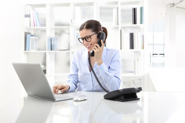 Una mujer que está atendiendo una llamada mientras mira el ordenador